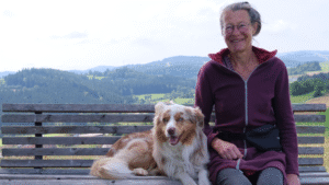 Wildblumen Karin Böhmer|Karin Böhmer sitzt mit ihrem Hund auf einer Bank in der Landschaft. Hinter ihr ist eine Landschaft mit Wildblumen und Hügeln zu sehen. Sie spricht über ihren Einsatz gegen das Artensterben auf unseren Wiesen.||Ein Foto von einer grünen Wiese mit vielen Wildblumen in verschiedenen Farben. Ein Symbol für den Kampf gegen das Artensterben.|Karin Böhmer mit einer Mitarbeiterin und der Journalistin Mira Dolleschka am Dachboden ihres Betriebs. Sie stehen auf Decken